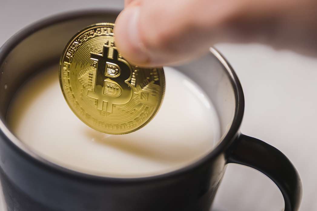 A person is pouring a crypto coin into a cup of milk, combining the worlds of NFT and DeFi.
