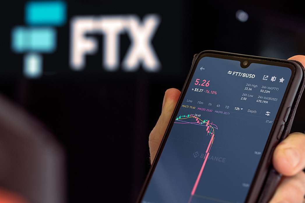 A person holding up a phone with the FTX logo on it, showcasing the cryptocurrency market and blockchain technology.