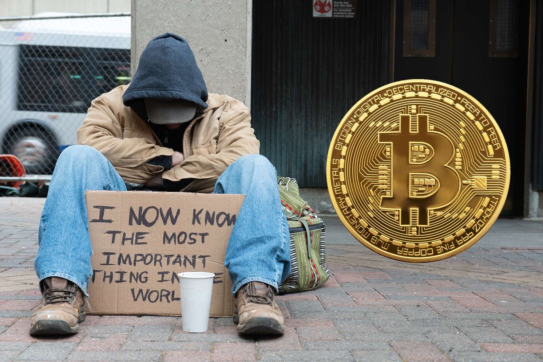 A homeless man sits on the sidewalk next to a bitcoin.