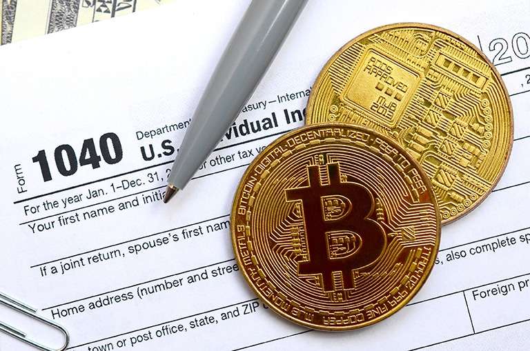 A pen and a bitcoin sit on top of a tax form, showcasing the interaction between traditional paperwork and the digital currency bitcoin.