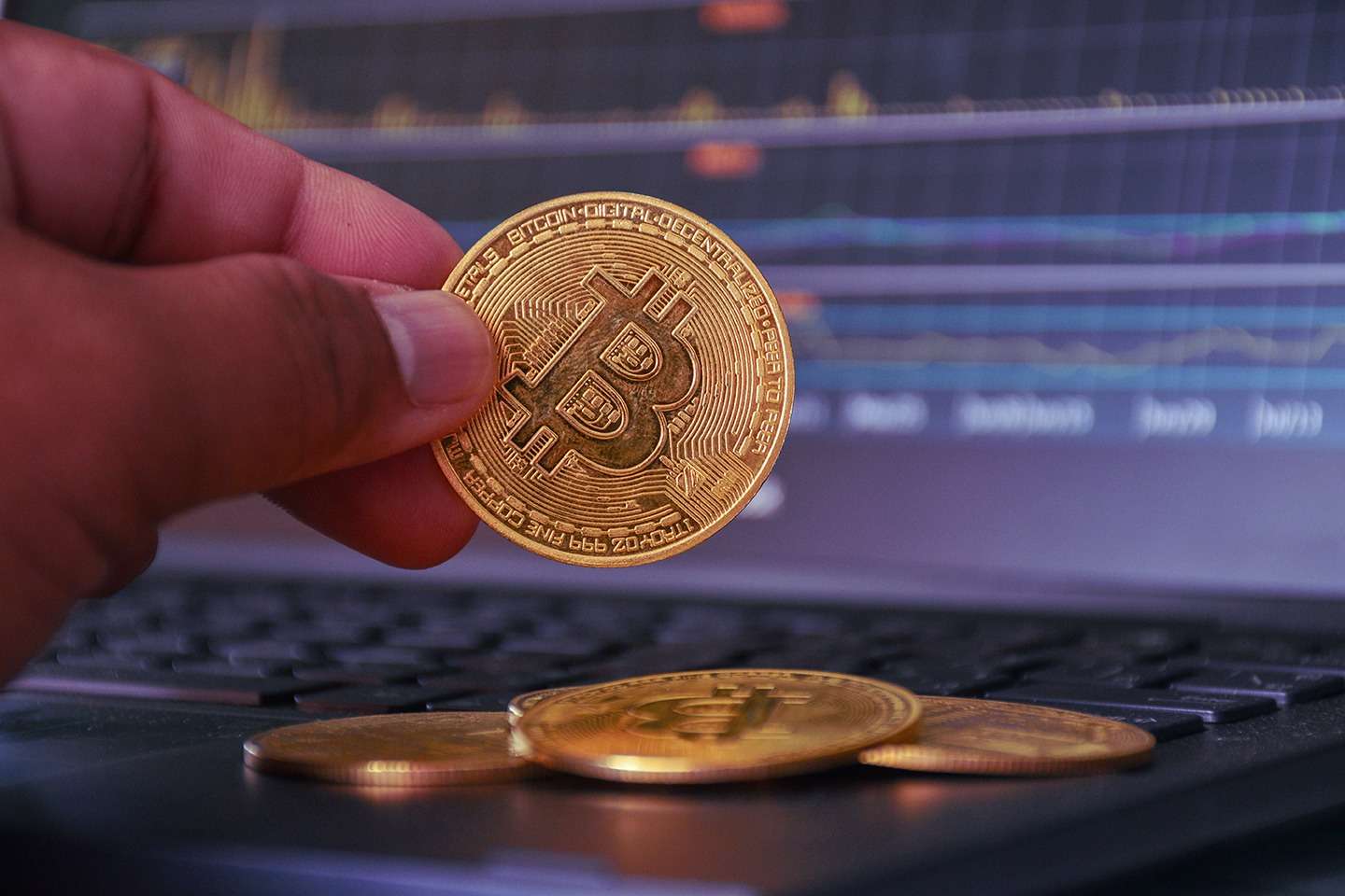 A person is holding a bitcoin in front of a laptop screen showcasing the power of blockchain technology.