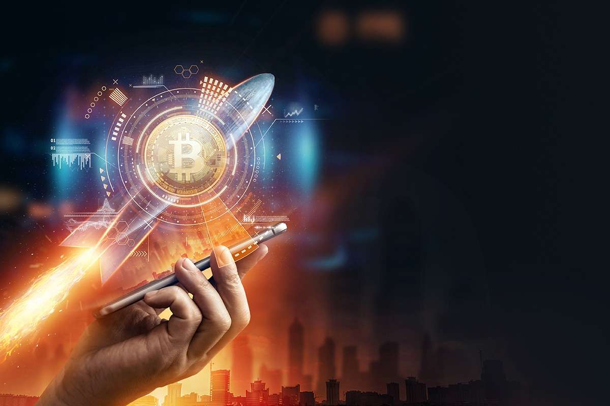 A hand holding a phone with a Bitcoin cryptocurrency in the background.