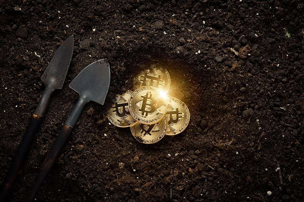 Bitcoins being mined as gold on a coal background with shovels.