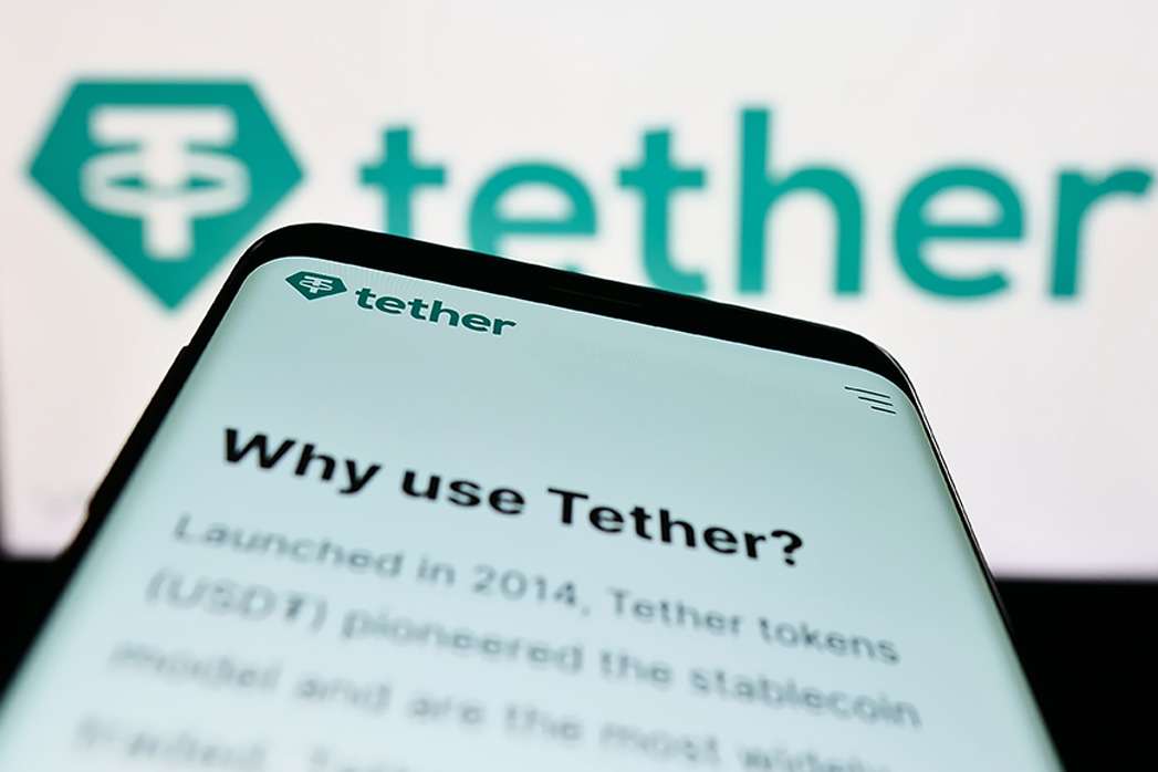 Smartphone with website of crypto company Tether Operations Limited on screen in front of business logo. Focus on top-left of phone display.