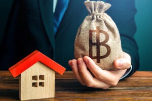 Man holds out a Bitcoin bag near the house.