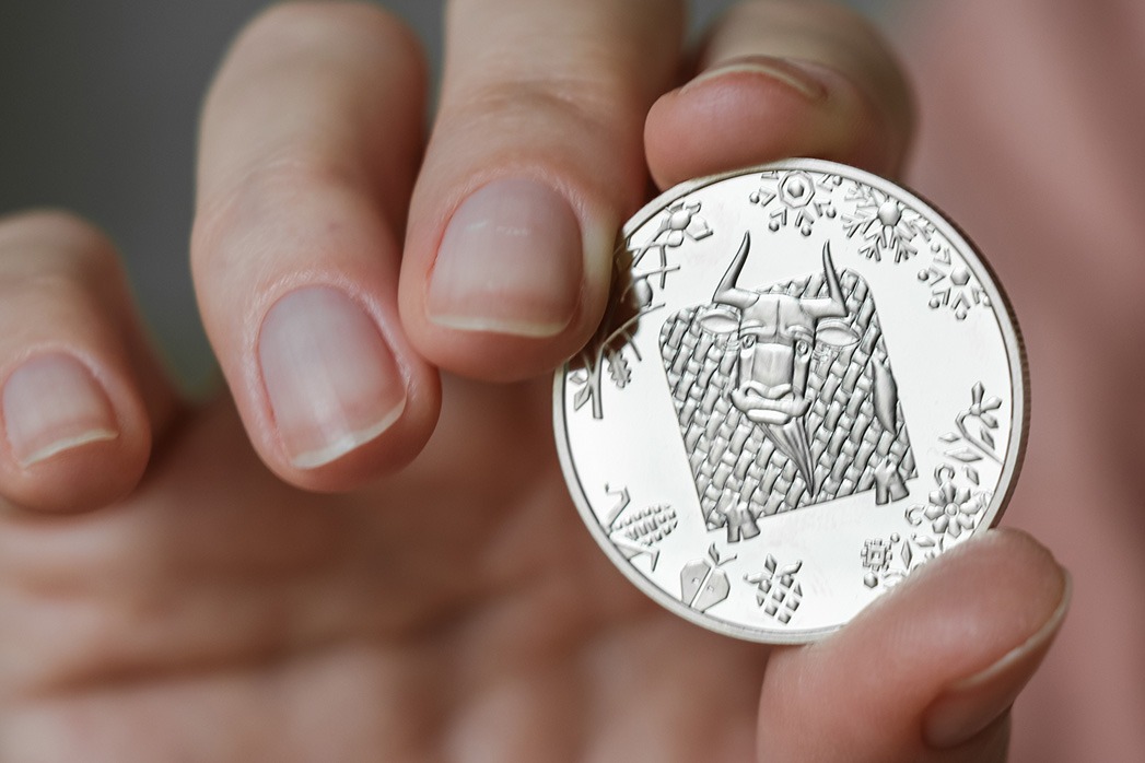 The person holds in his hand a commemorative coin dedicated to the year of the bull.