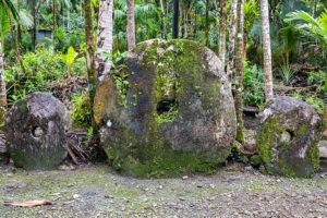 Three giant prehistoric megalithic stone coins or money Rai, under trees overgrown in jungle. Yap island, Federated States of Micronesia, Oceania, South Pacific Ocean.