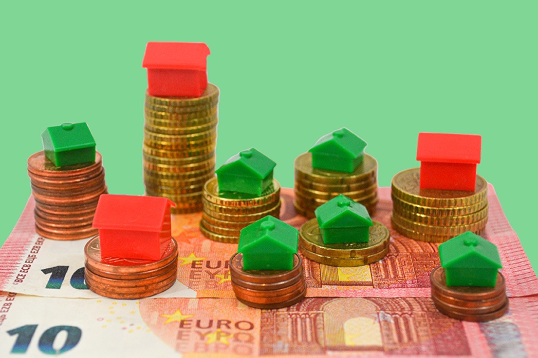 Heap of coins with a house plastic icon on Euro banknotes, isolated on green background.
