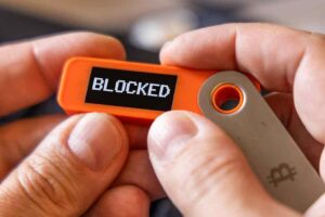 A hardware Bitcoin wallet held in white hands with a blocked message on the screen.