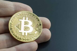 Owning bitcoin investment symbolized by a hand holding a real bitcoin. Buying and investing in BTC crypto-currency.