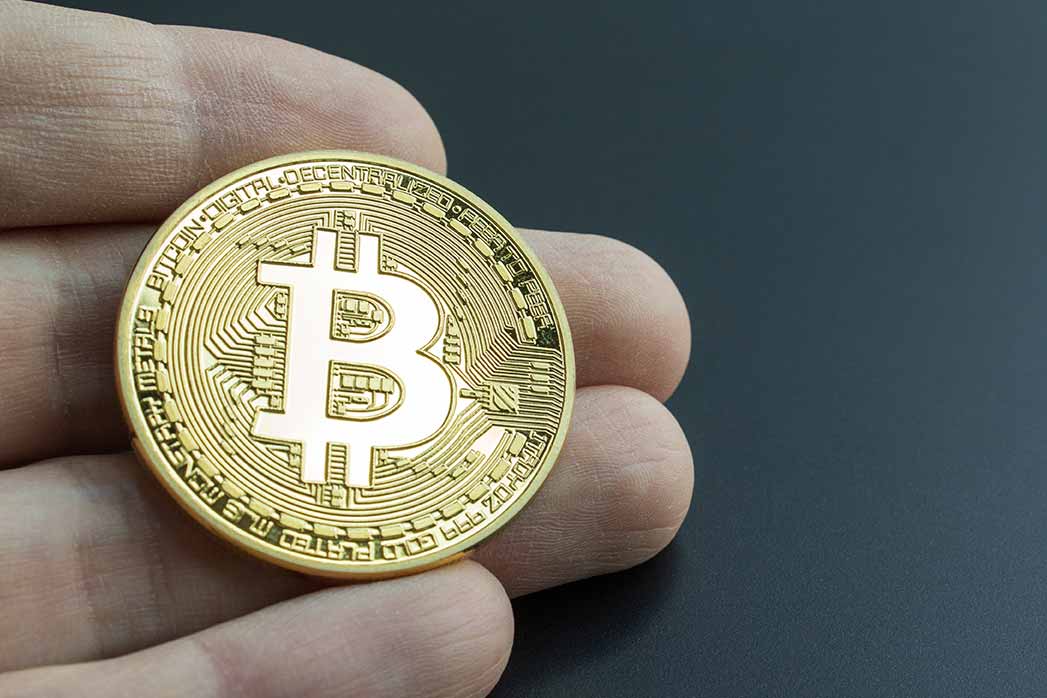 Owning bitcoin investment symbolized by a hand holding a real bitcoin. Buying and investing in BTC crypto-currency.