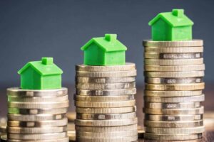 Green Toy Houses on Stacks of Shiny Coins.