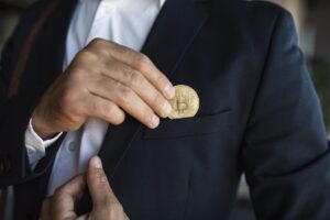 Male ceo manager in suit putting bitcoin coin in pocket, standing in office interior, closeup.